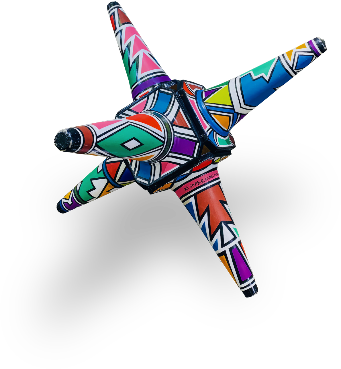 A colourful, geometric star-shaped sculpture with five pointed arms, each decorated in bold, intricate patterns of red, blue, green, orange, yellow, purple, black and white. The patterns feature zigzags and diamonds. The background is transparent.