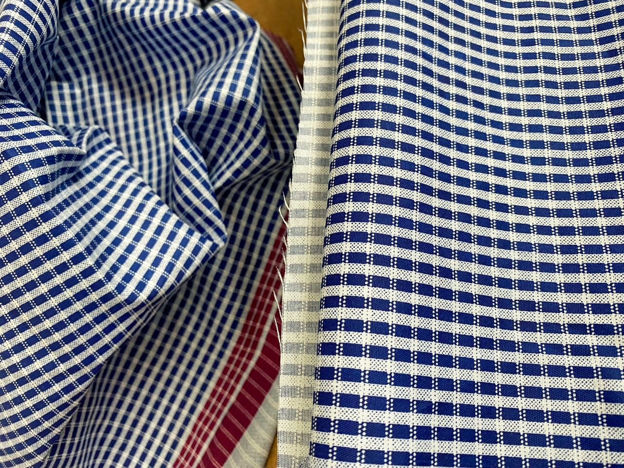 Several pieces of fabric in different colours feature a small, chequered pattern. Visible are blue, red, grey, and dark blue cloths, each with alternating squares and stripes, neatly arranged and some slightly creased where they overlap.