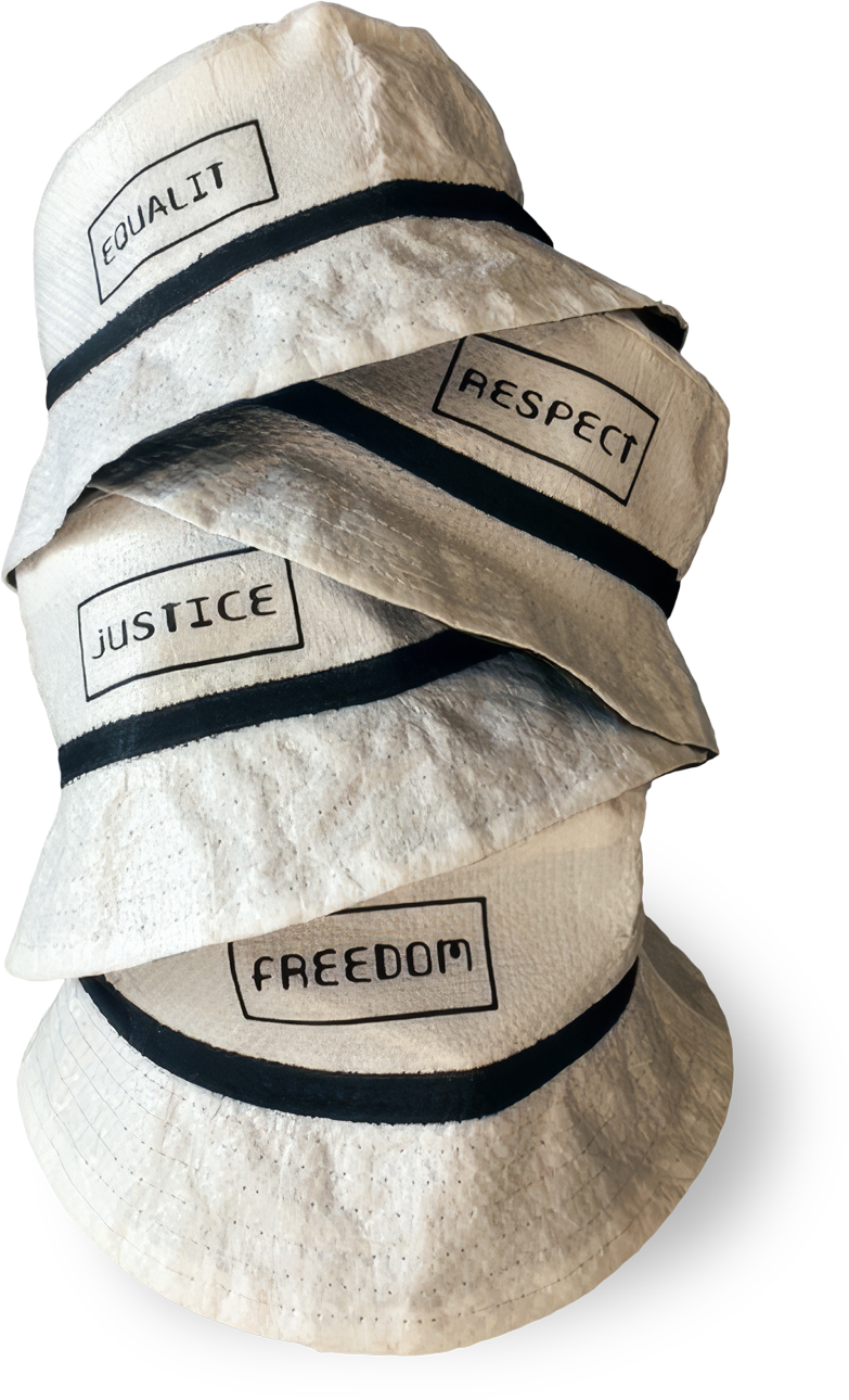 Four white bucket hats with black bands are stacked vertically. Each hat has a different word in black capital letters within a rectangle: “EQUALITY”, “RESPECT”, “JUSTICE”, and “FREEDOM”. The background is black.