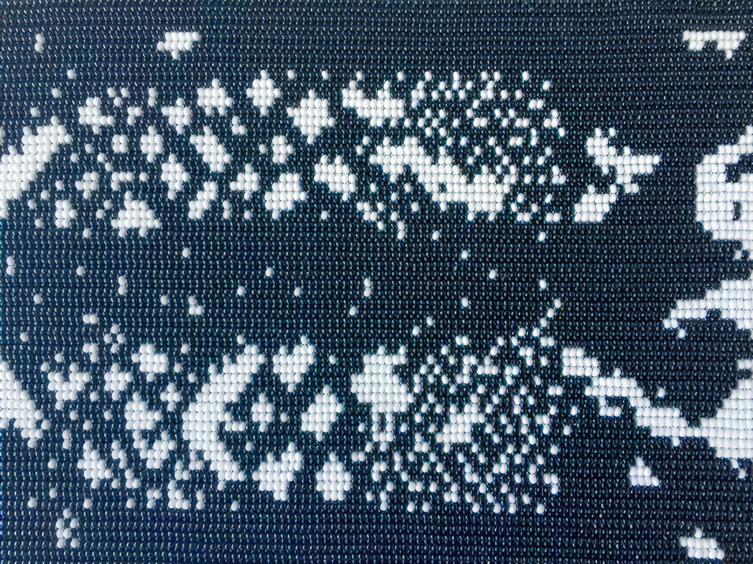 Close-up of a mosaic made from small, round, shiny beads arranged on a grid. The beads form an abstract black and white pattern with scattered clusters that create a high-contrast, pixelated effect, resembling a digital image or code.
