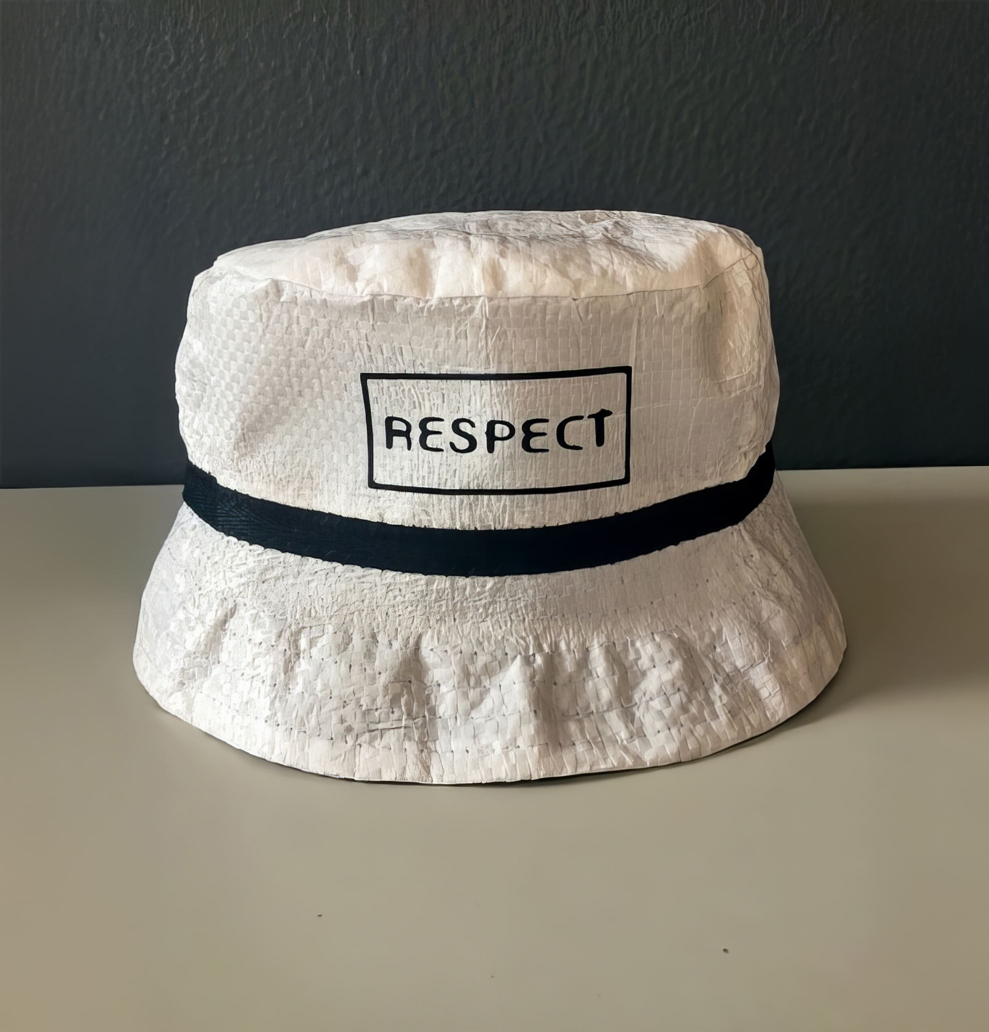 A white bucket hat with a black horizontal stripe and a rectangular label on the front displaying the word 