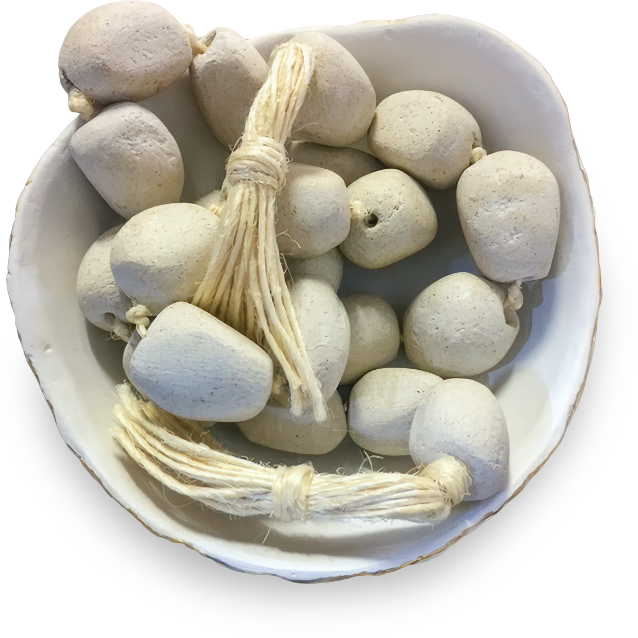 A white bowl contains several smooth, pale grey stone beads. Some beads are strung together with natural, thick, tan twine tied in knots, while others are loose. The bowl and beads have a handmade, rustic appearance.