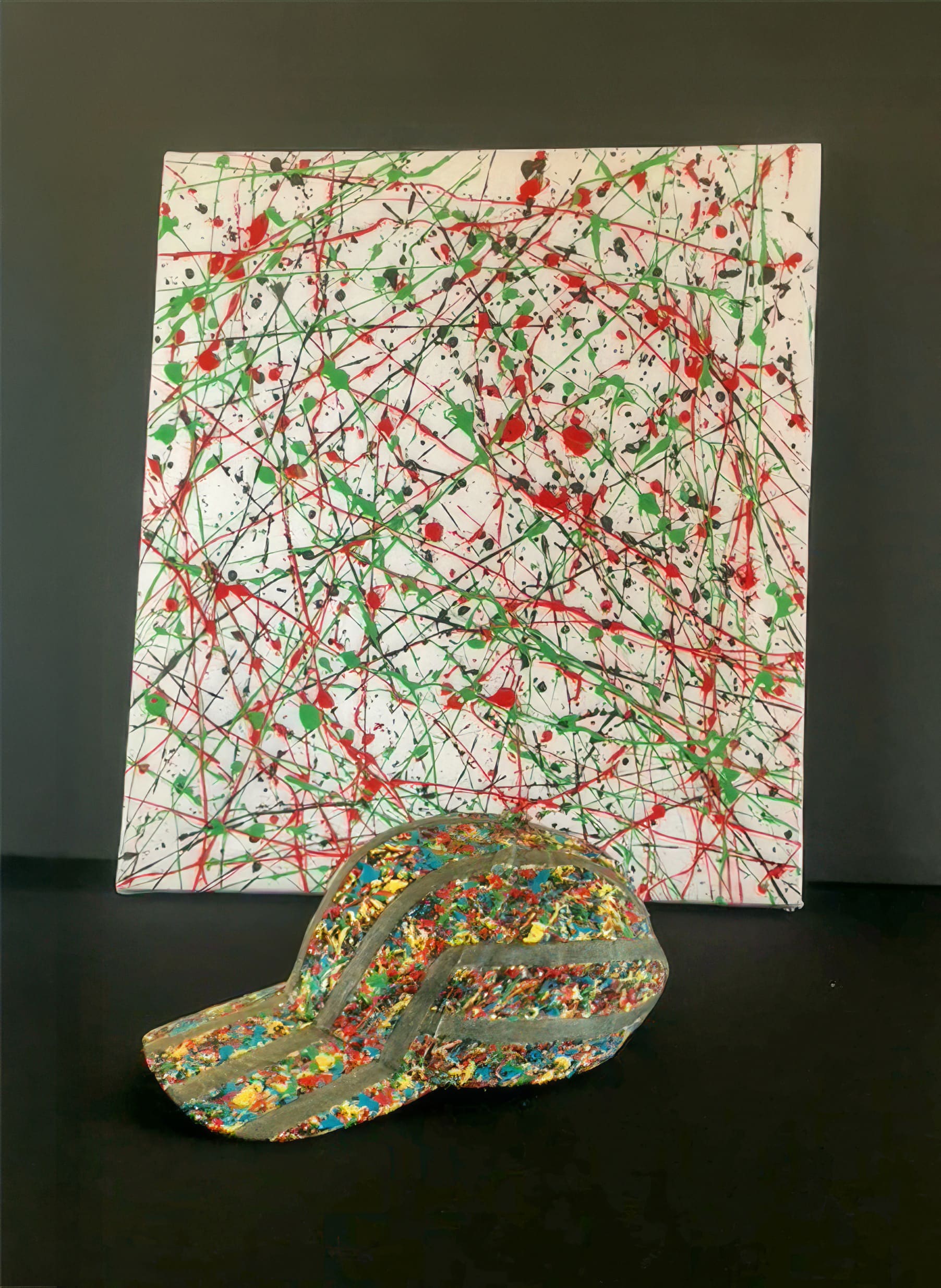 A colourful baseball cap with splattered paint patterns sits on a dark surface in front of a canvas featuring abstract, splattered lines and spots in red, green, and black on a white background. Both items have a vibrant, chaotic, Jackson Pollock-like style.