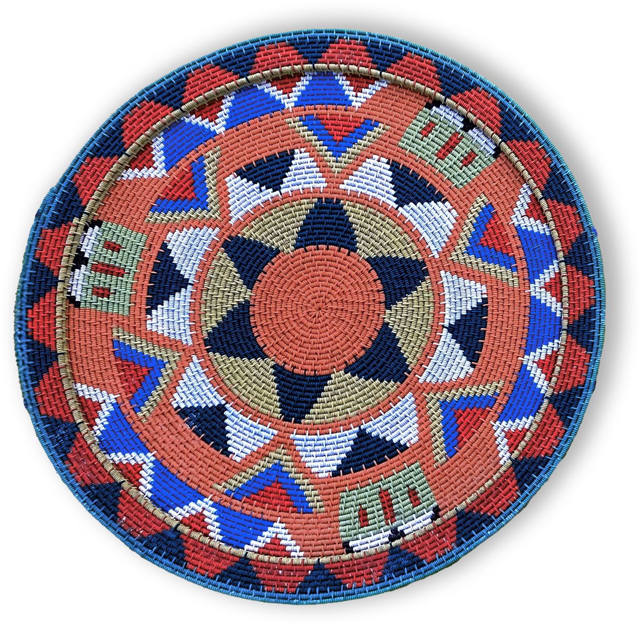A round, woven basket lid with a geometric pattern in red, blue, tan, white, green, and black. It features star shapes, triangles, and rectangles, all arranged symmetrically around the centre, with a braided blue edge. The background is black.