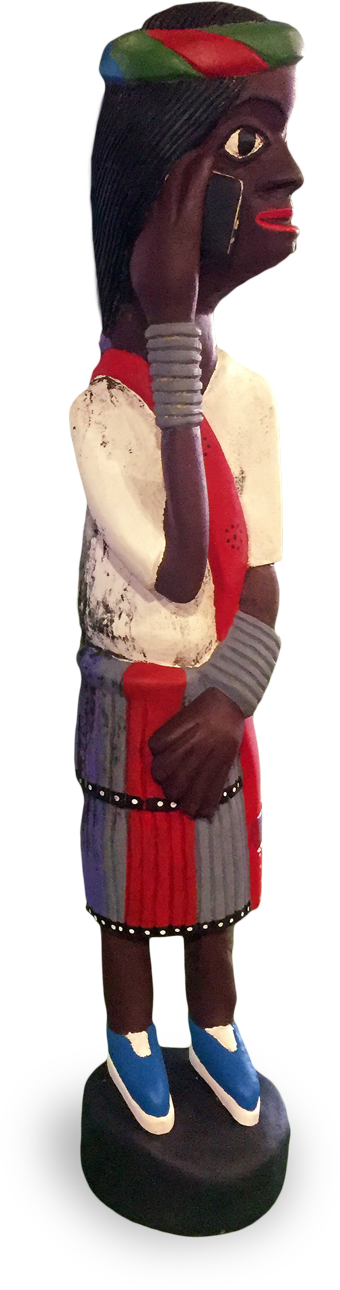 A painted wooden figurine of a woman with dark skin, wearing a colourful skirt, red scarf, blue shoes, and metal bangles. She holds a black mobile phone to her ear, and her hair is covered by a green and red headscarf.