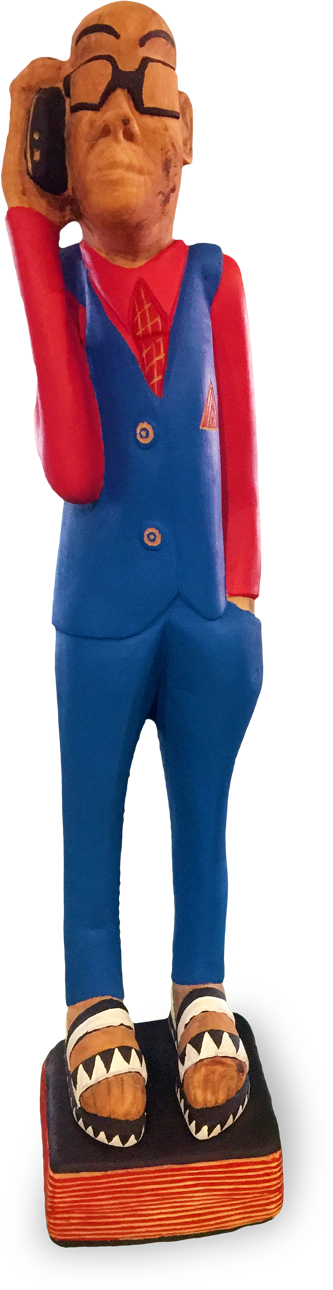 A colourful wooden sculpture of a person in a blue suit, red shirt, and tie, wearing glasses, holding a black phone to their ear, and standing on a striped base with patterned shoes. The figure has exaggerated facial features and a stylised appearance.