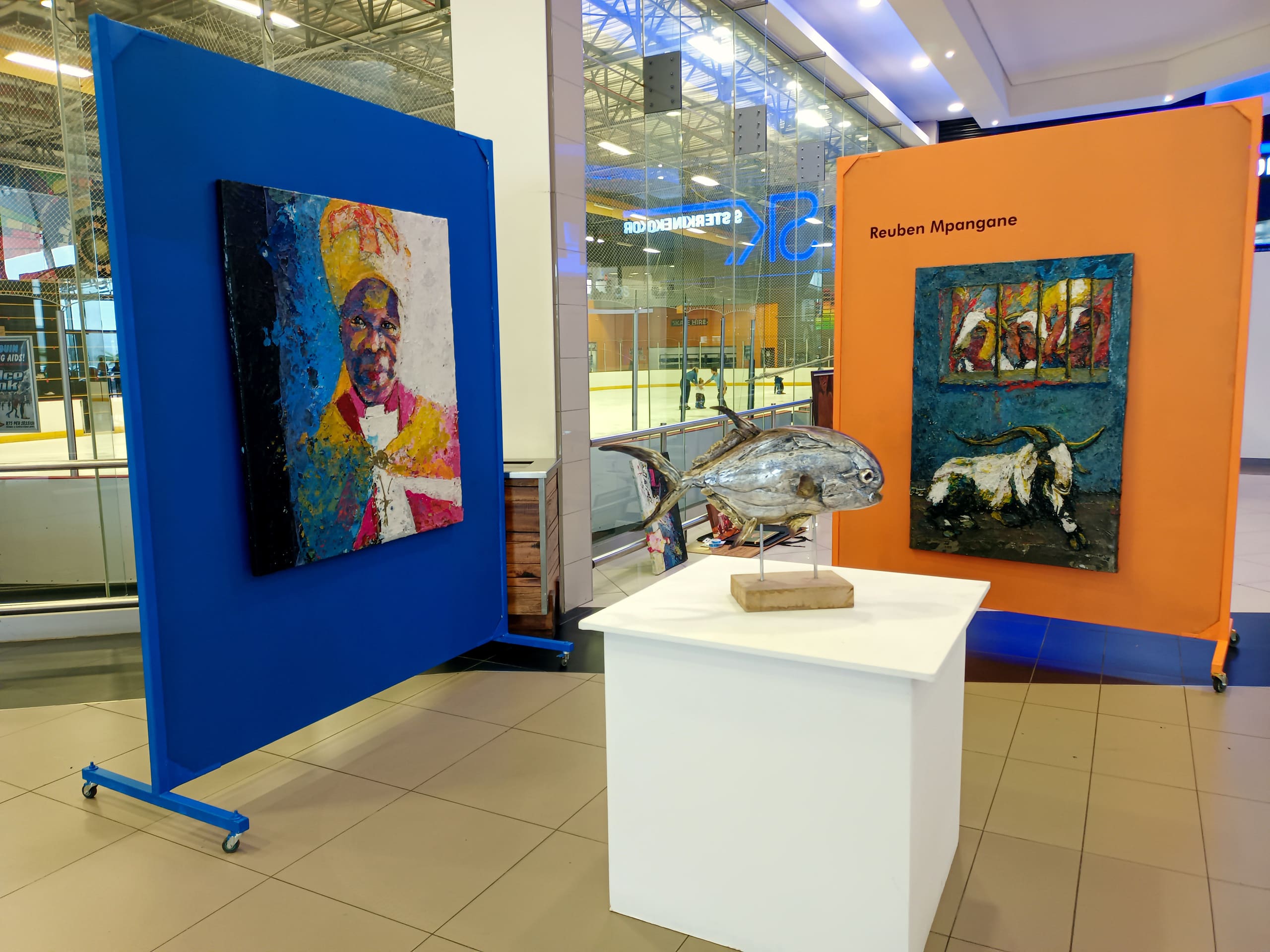Two colourful art panels are displayed in a shopping centre, one blue with a textured portrait and one orange labelled 