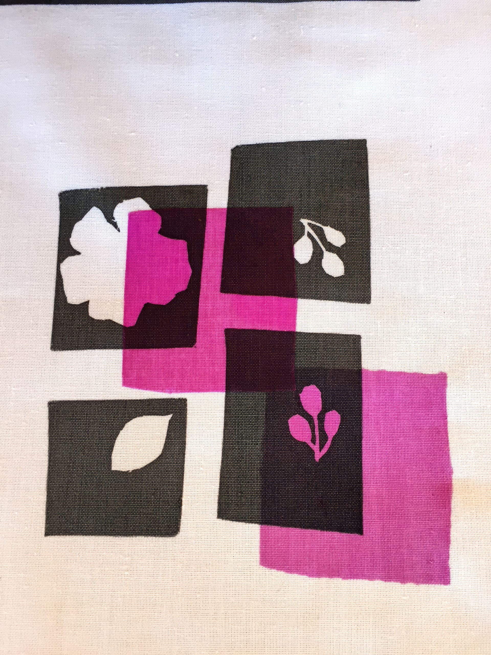 A fabric with a geometric pattern of dark grey and magenta squares, some overlapping. Each square features simple white botanical silhouettes: a leaf, a flower, and two twig-like branches with berries, set against a white background.