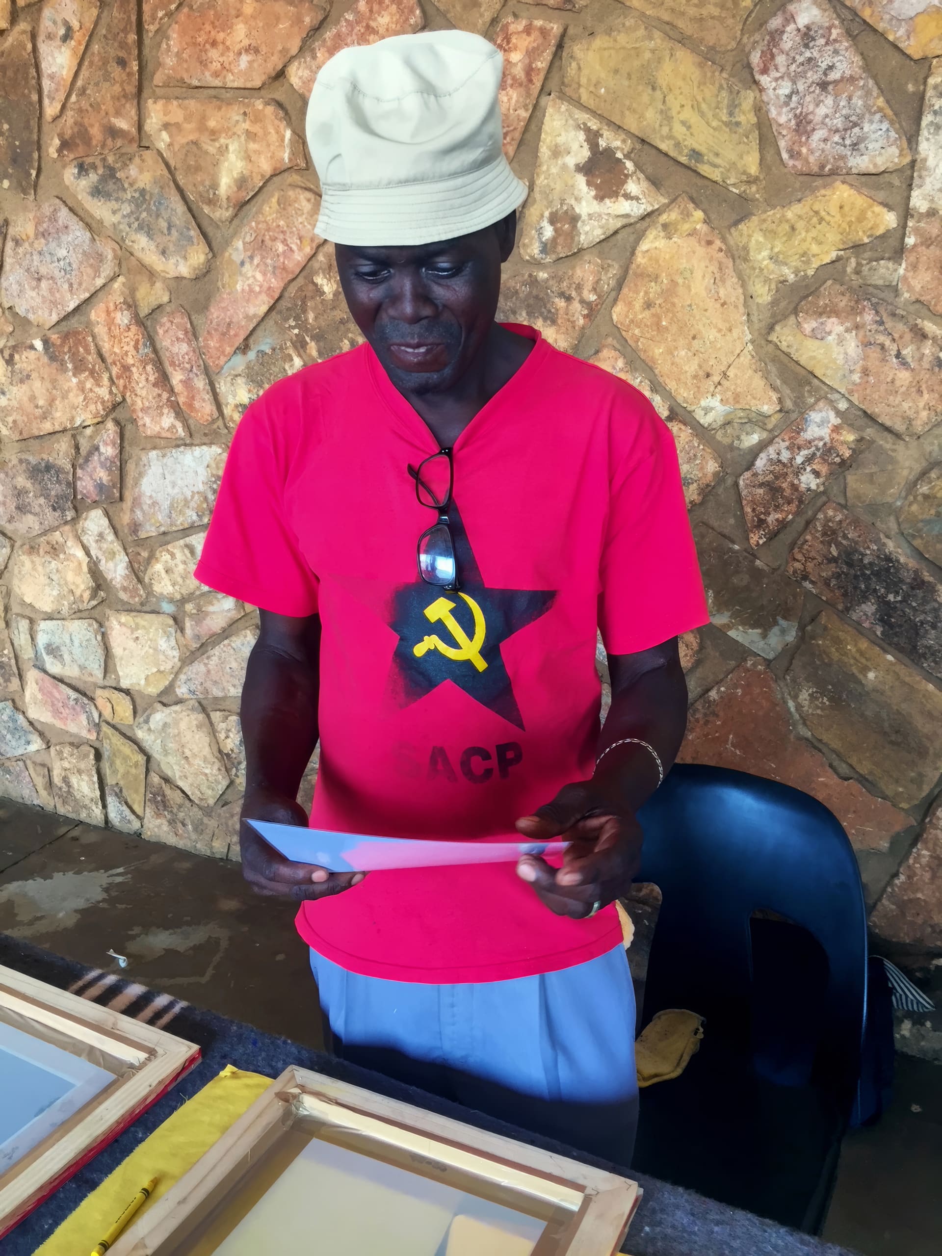 A man wearing a beige bucket hat, a red T-shirt with a black star, yellow hammer and sickle, and 