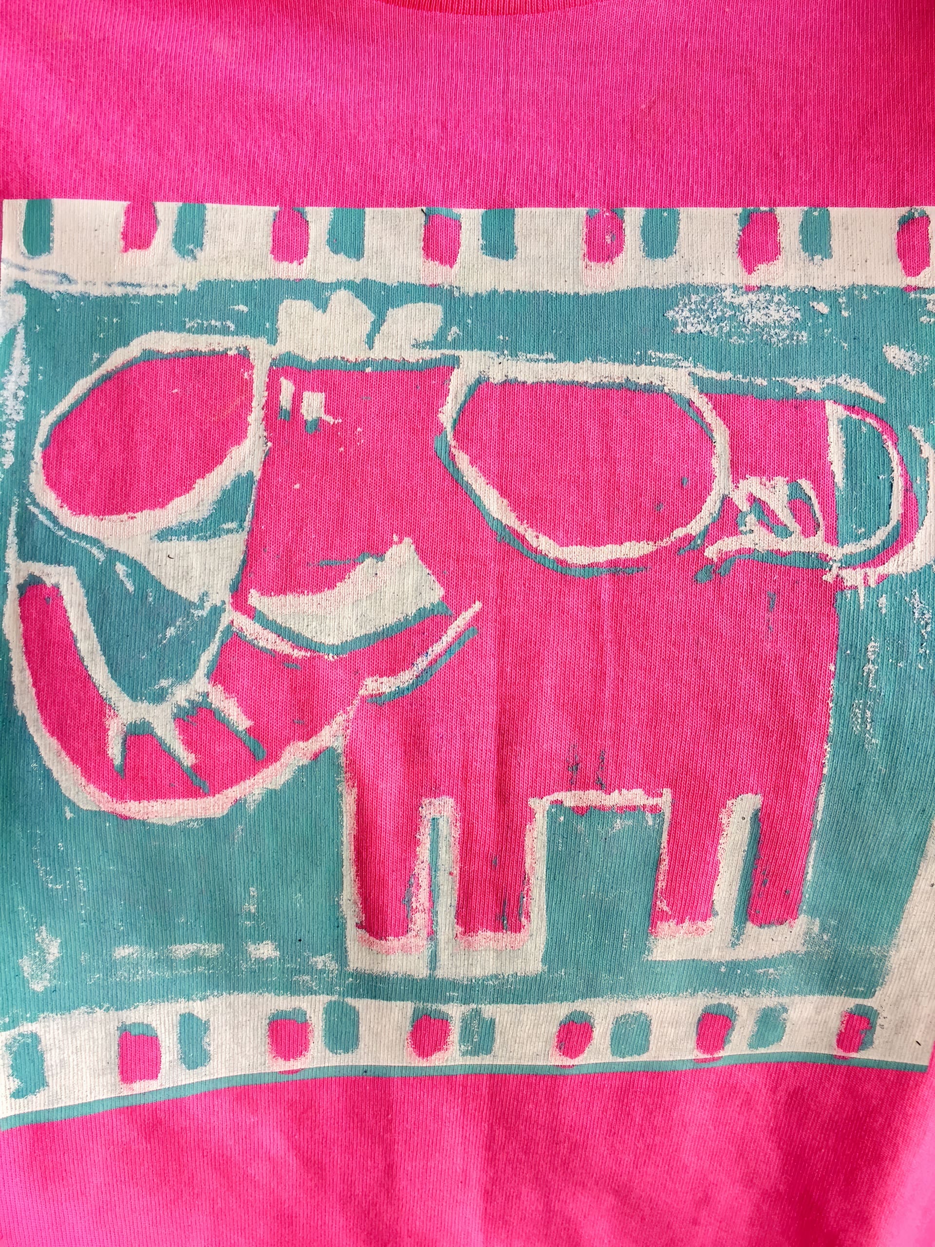 A stylised, block-print illustration of a pink elephant with an upraised trunk is centred on a bright pink background, framed by a turquoise and white patterned border. The image has a playful, childlike, and abstract feel.