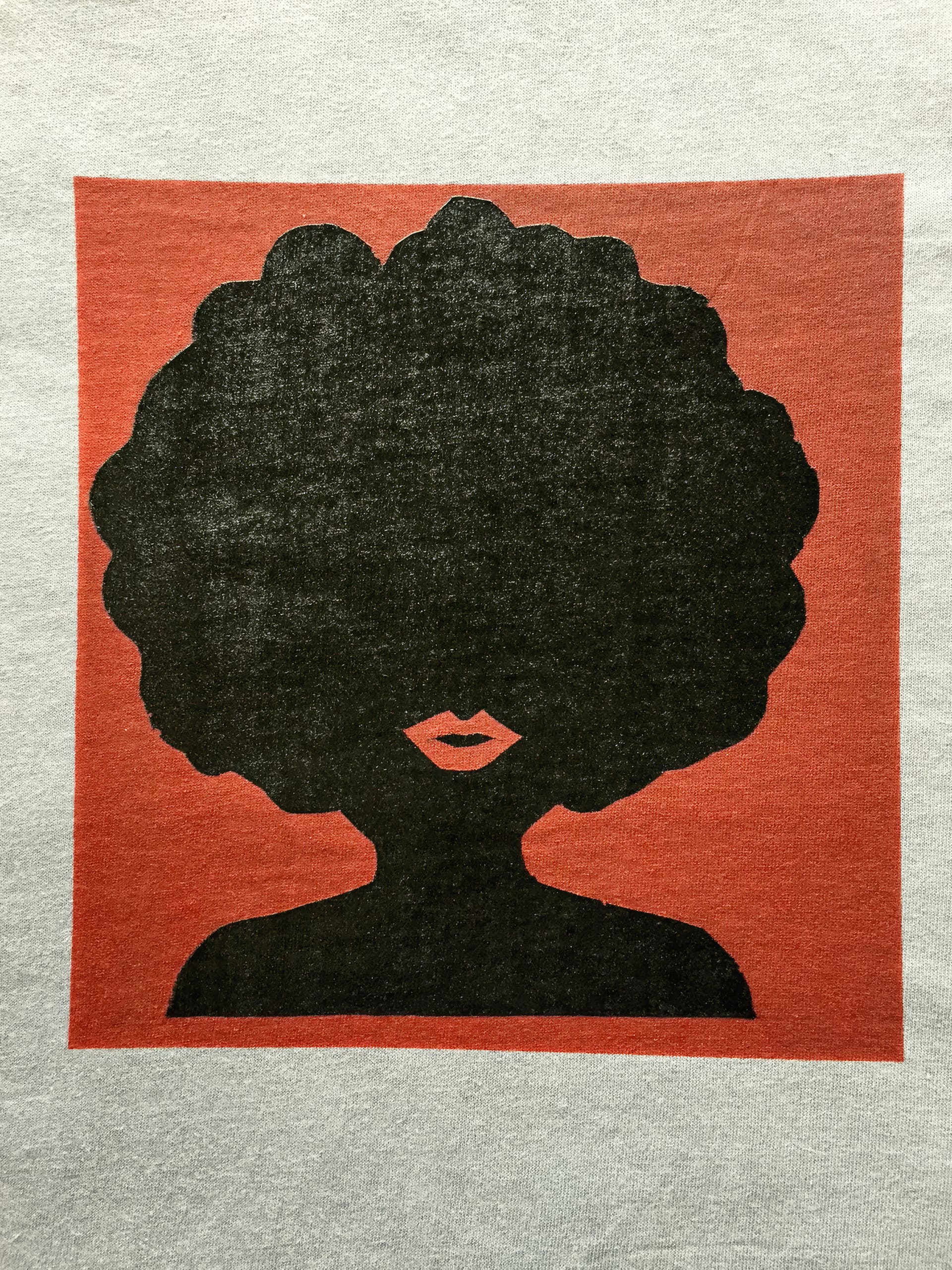 A minimalist silhouette of a person with a large afro hairstyle, red lips, and no visible facial features. The figure is centred in a red square against a grey background, with bold black for the hair and upper body.
