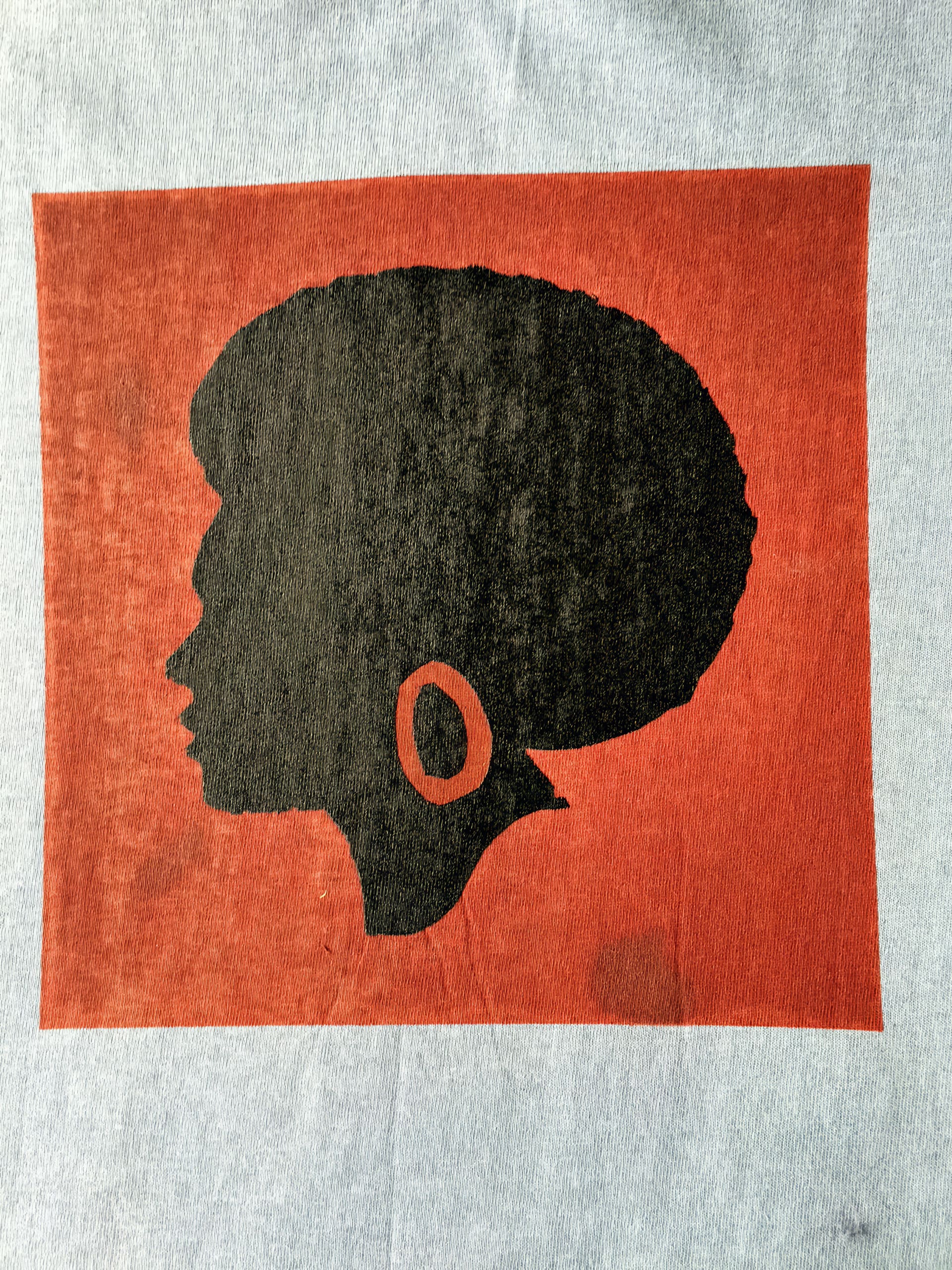 A black silhouette of a woman’s head in profile with an Afro hairstyle and a large hoop earring, set against a solid red square on a light grey background.