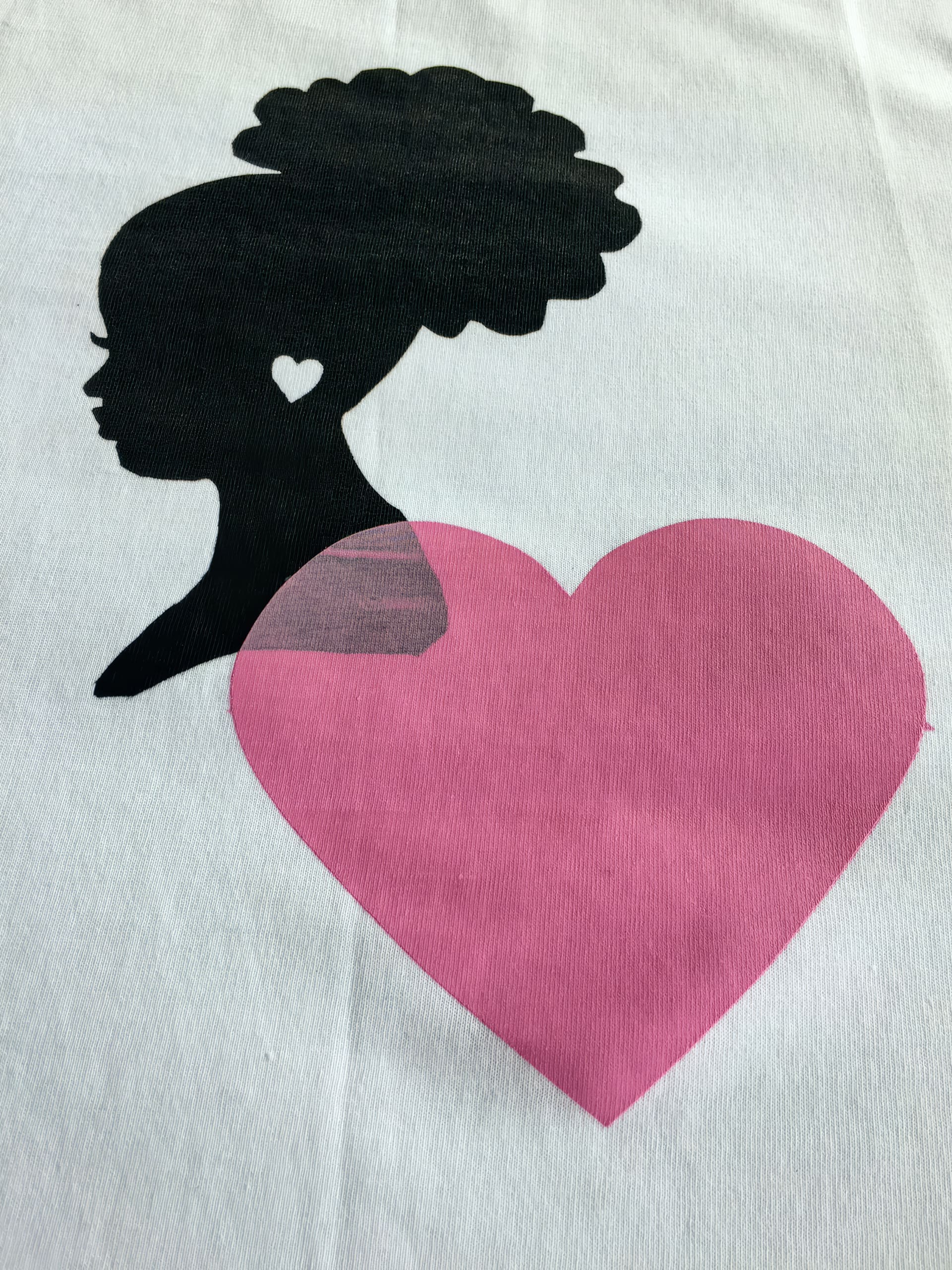 A black silhouette of a woman in profile with curly hair in a bun and a heart-shaped earring is shown above a large pink heart, all on a white background.