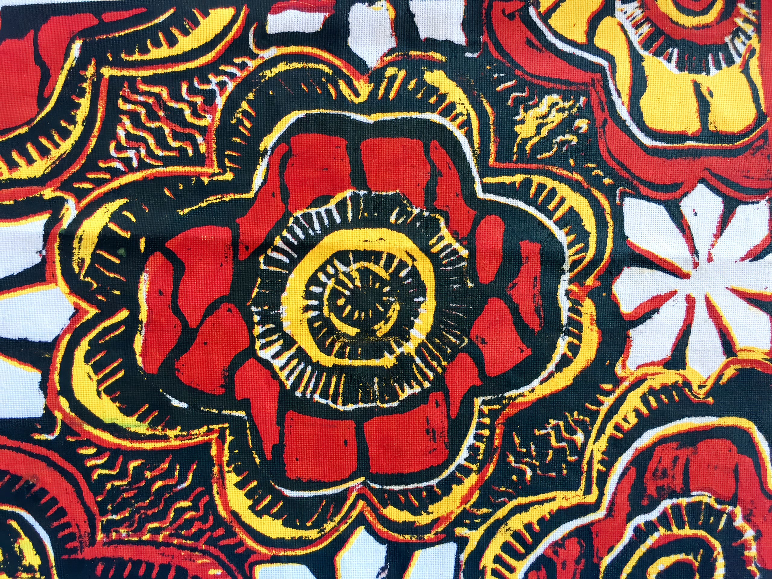 A vibrant abstract pattern features bold, swirling flower shapes in red, yellow, black, and white. The central large flower has concentric layers with radiating lines, surrounded by intricate textures and smaller repeating floral motifs.