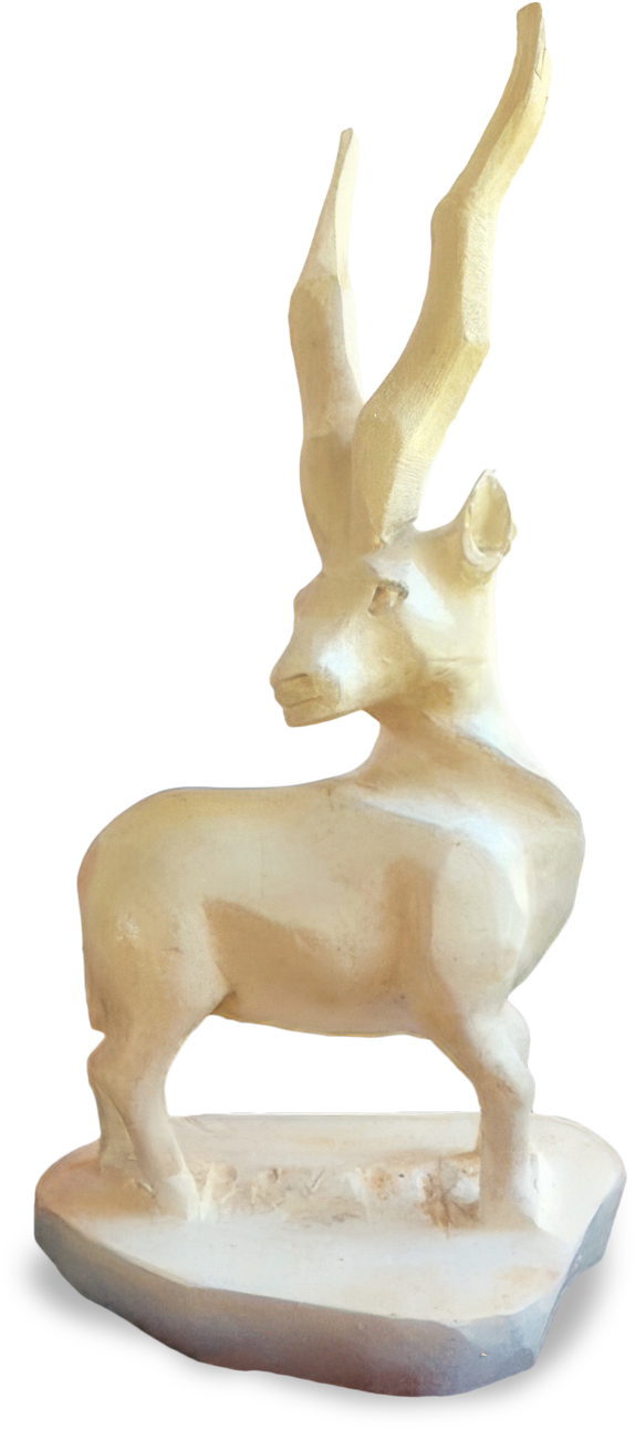 A light-coloured, roughly-carved wooden sculpture of an antelope stands on a flat base. The antelope has long, spiralled horns and is depicted in a static pose, facing left. The background is plain and has shades of beige and black.