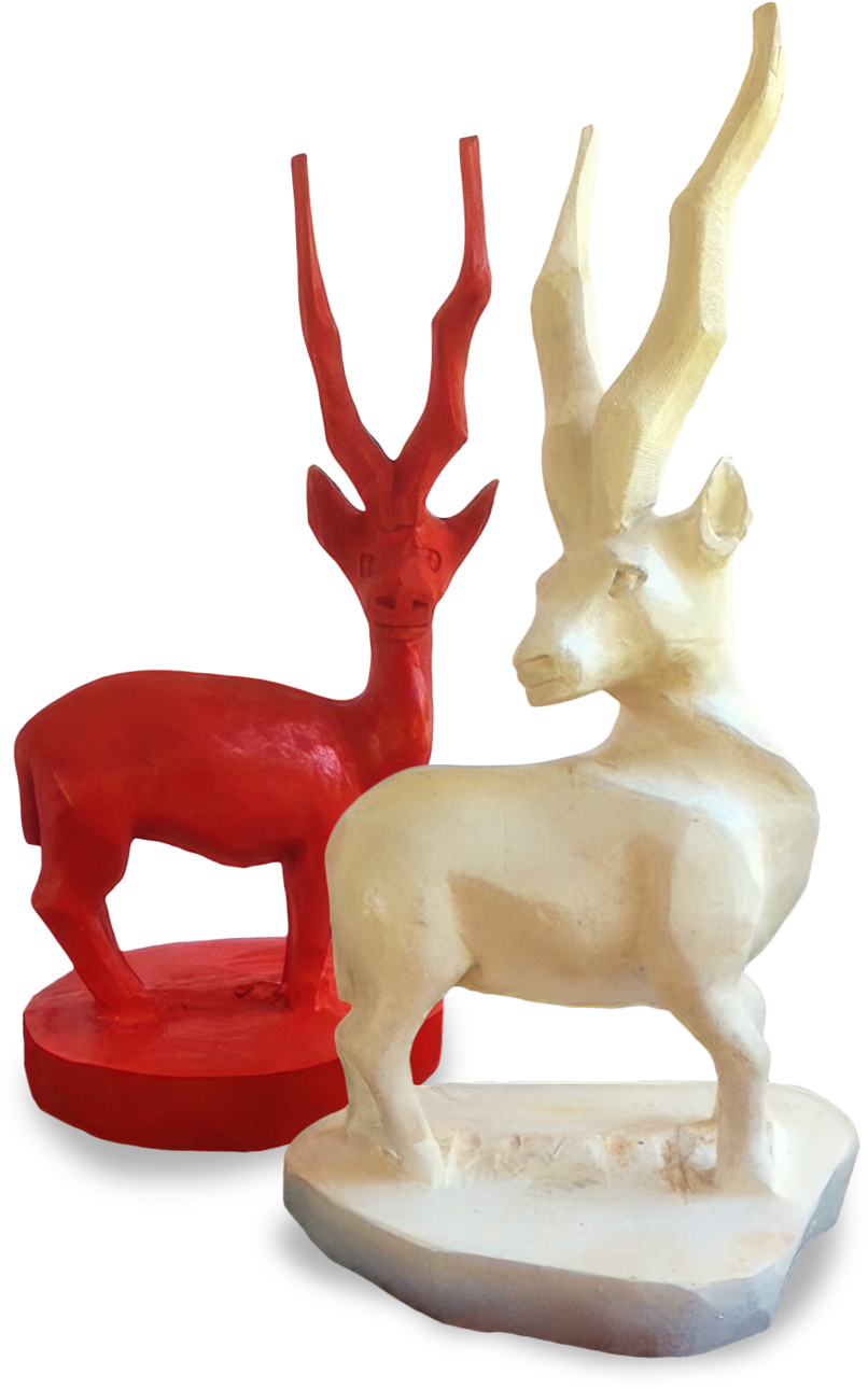 Two stylised antelope sculptures stand side by side. The figure in front is off-white with long, curved horns and angular features. The figure behind is bright red, slightly smaller, with similar elongated horns and a rounded base.