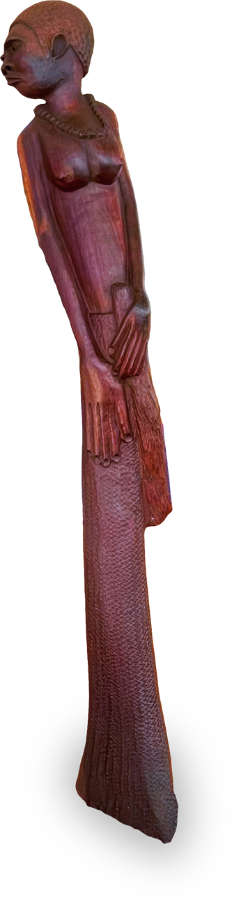 A tall, slender wooden sculpture of a woman with a beaded necklace, stylised facial features, elongated arms, and a textured long skirt; her hands are posed together at her waist, and she gazes to the side with a serene expression.