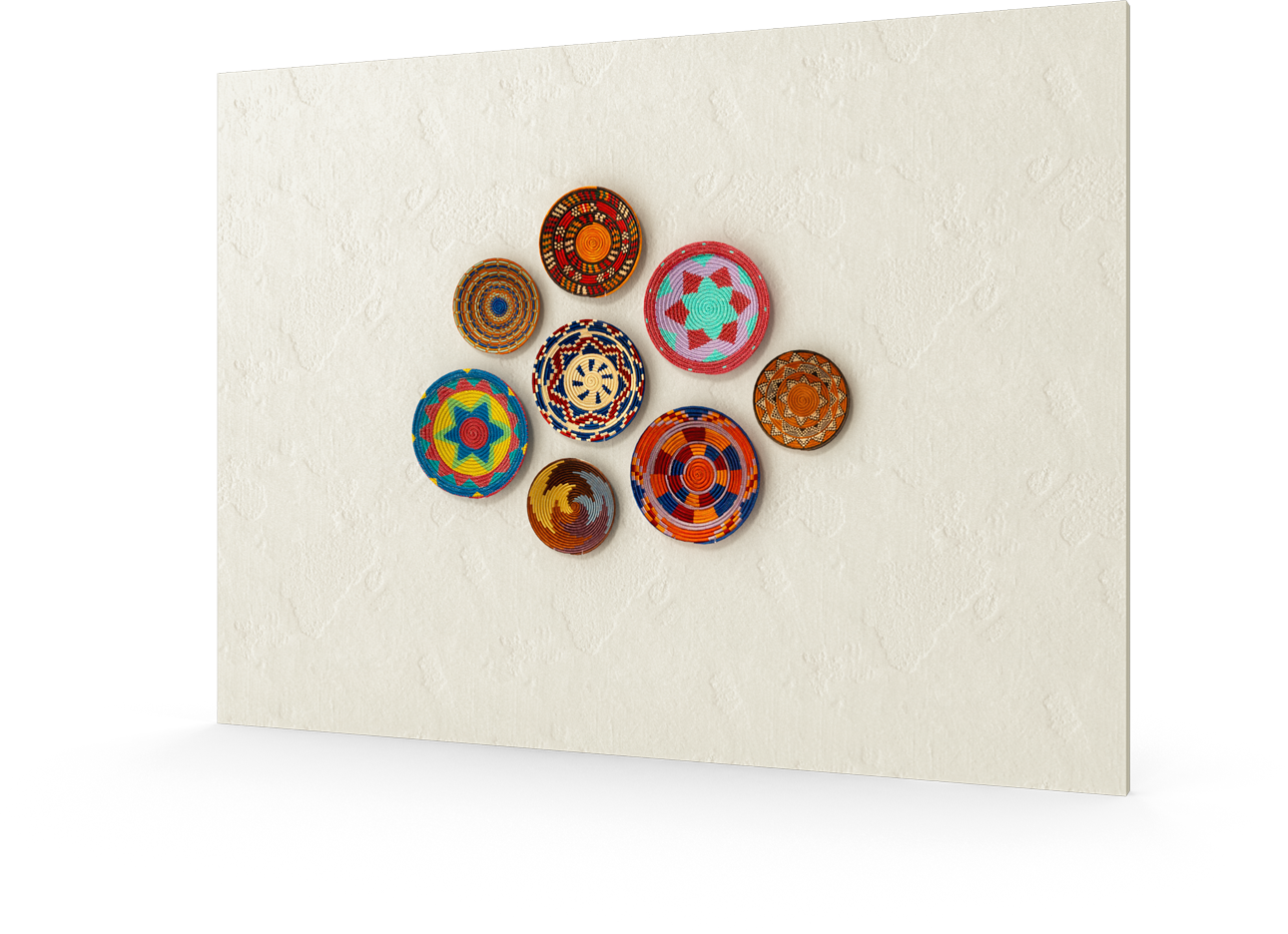 Eight colourful, round, woven baskets with geometric patterns and various shades of orange, blue, red, and yellow are arranged in a circular cluster on a textured, off-white wall. The baskets are evenly spaced and symmetrically displayed.