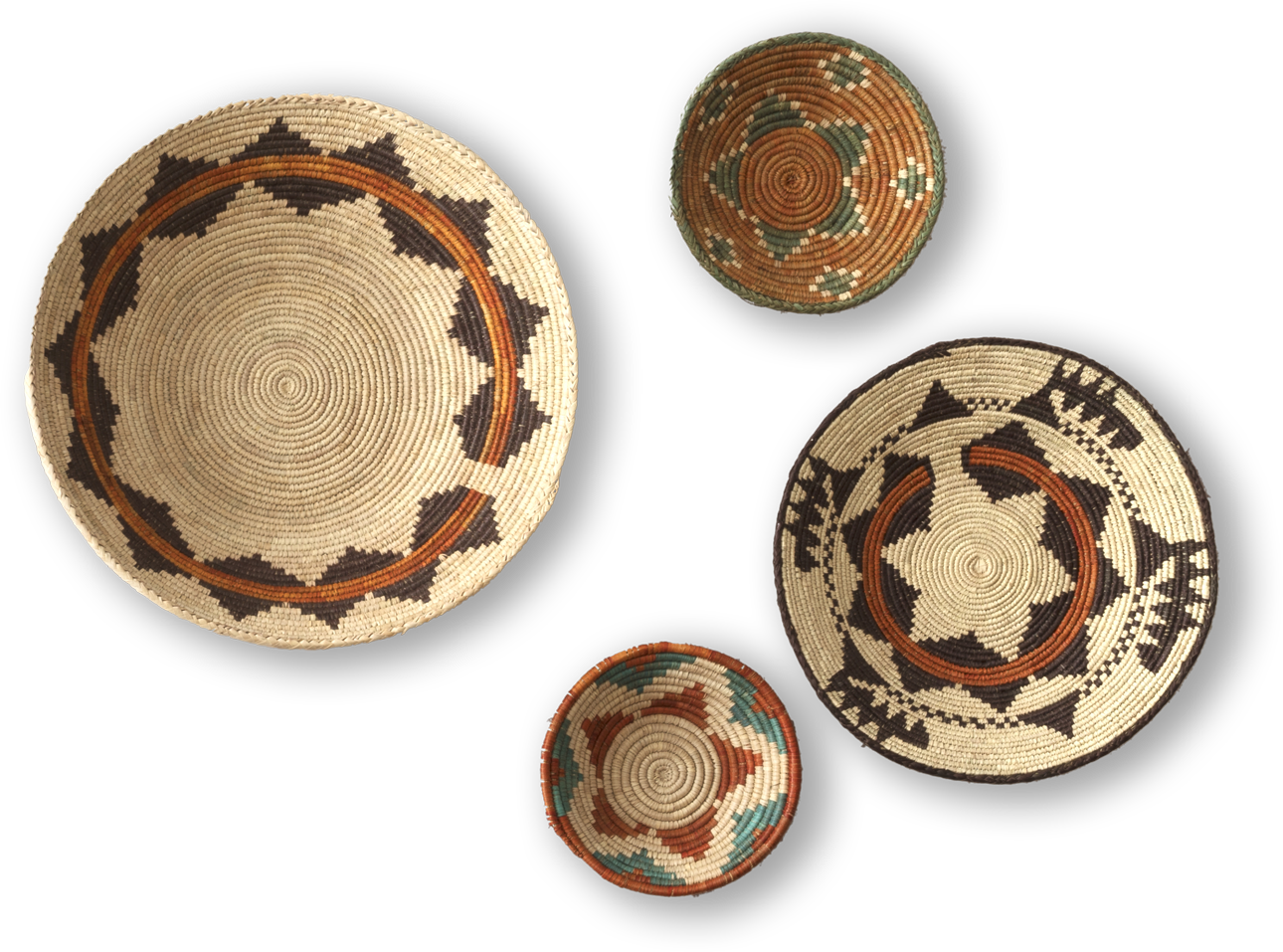 Four round, woven baskets with intricate geometric patterns in earthy tones—tan, brown, black, green, and orange—are displayed against a black background. The baskets vary in size, with two large and two smaller ones arranged asymmetrically.