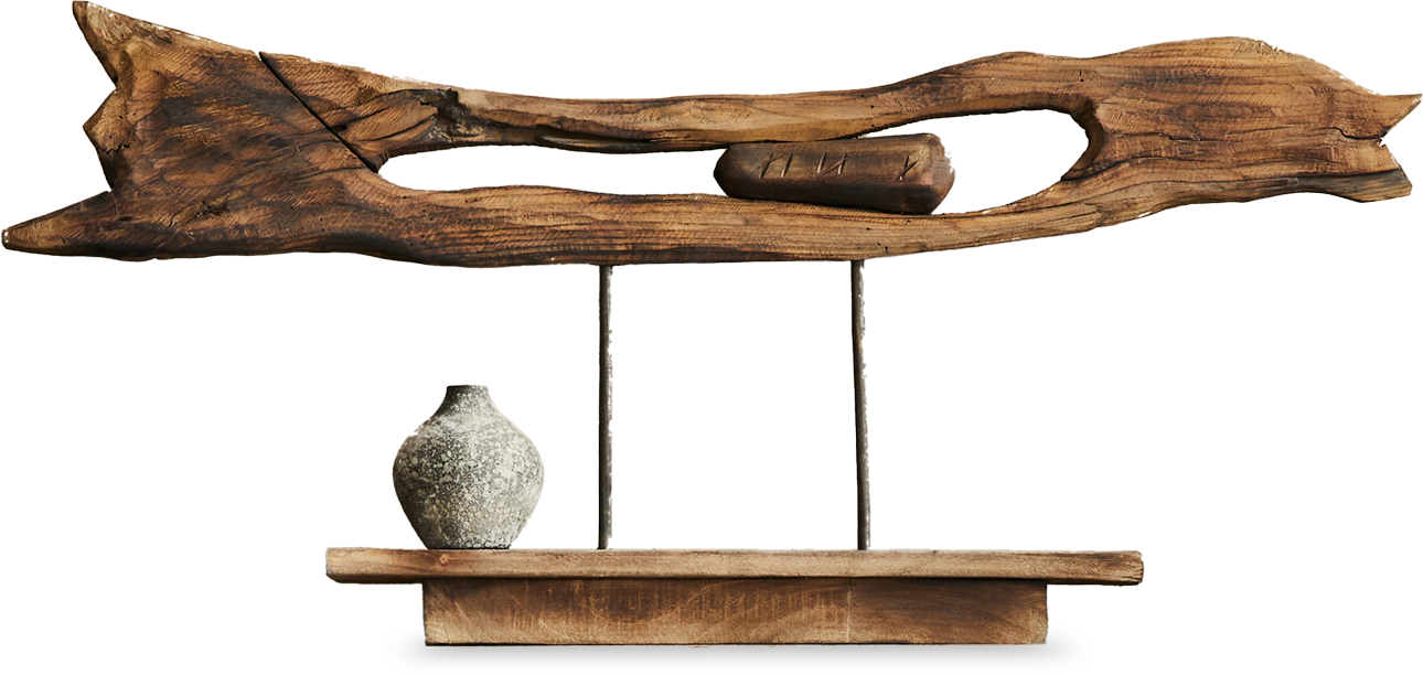 A decorative wooden sculpture features a large, weathered piece of driftwood mounted horizontally above a small rustic shelf. A round, textured ceramic vase sits on the left side of the shelf, and a small log is displayed within the wood’s hollow centre.