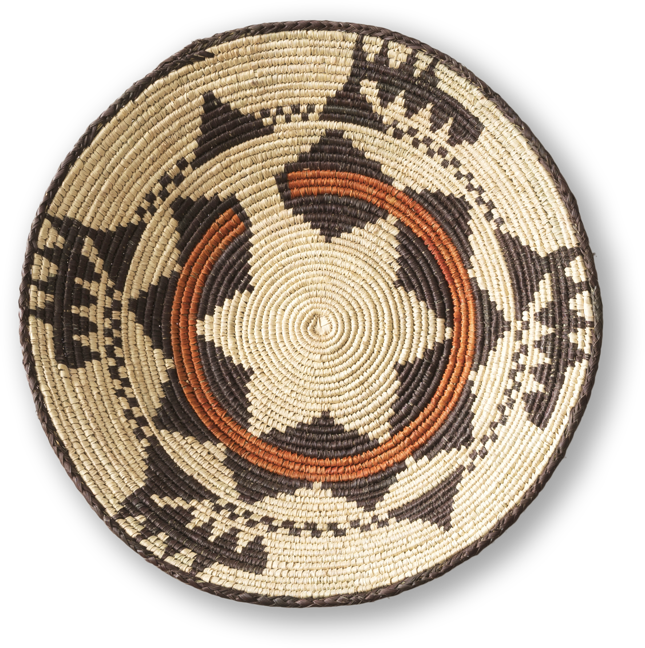 A round, woven basket lid features intricate black and tan geometric patterns and two curved orange bands. The design forms a star shape at the centre, with repeating triangles and zigzags along the edges. The basket has a coiled, textured appearance.
