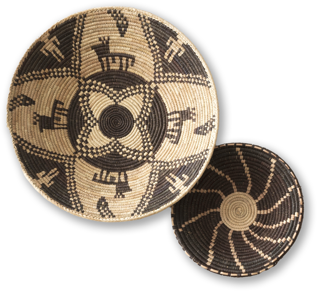 Two round, woven baskets with intricate patterns sit overlapping. The larger basket features black and cream geometric and animal designs, whilst the smaller one displays a spiralling black and cream pattern. Both have tight, detailed weaving.
