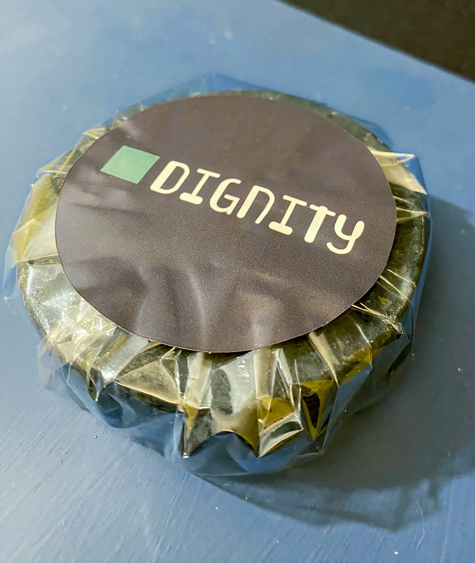 A round item wrapped in clear plastic with a black label on top displaying the word 