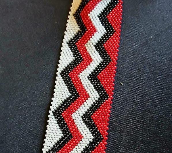 A beaded bracelet with a zigzag pattern in red, white, and black beads. Inspired by Contra.Joburg’s bold style, the dense beadwork and angular lines create a striking visual effect—echoing the intricate Weight of Silence motif.