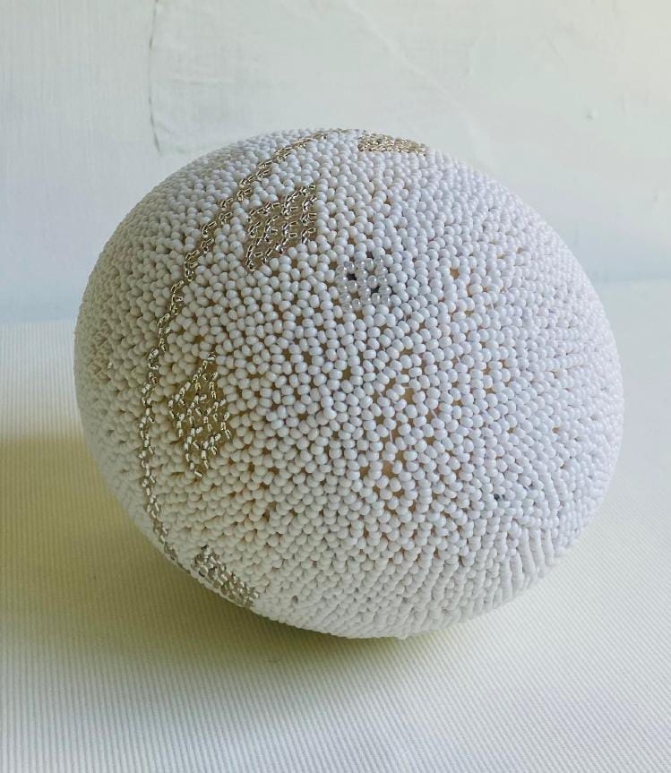A round, white textured ball covered in small, bead-like bumps sits on a light surface. Subtle gold lines form diamond-shaped patterns, echoing the intricate artistry of Contra.Joburg and the quiet depth found in Weight of Silence.