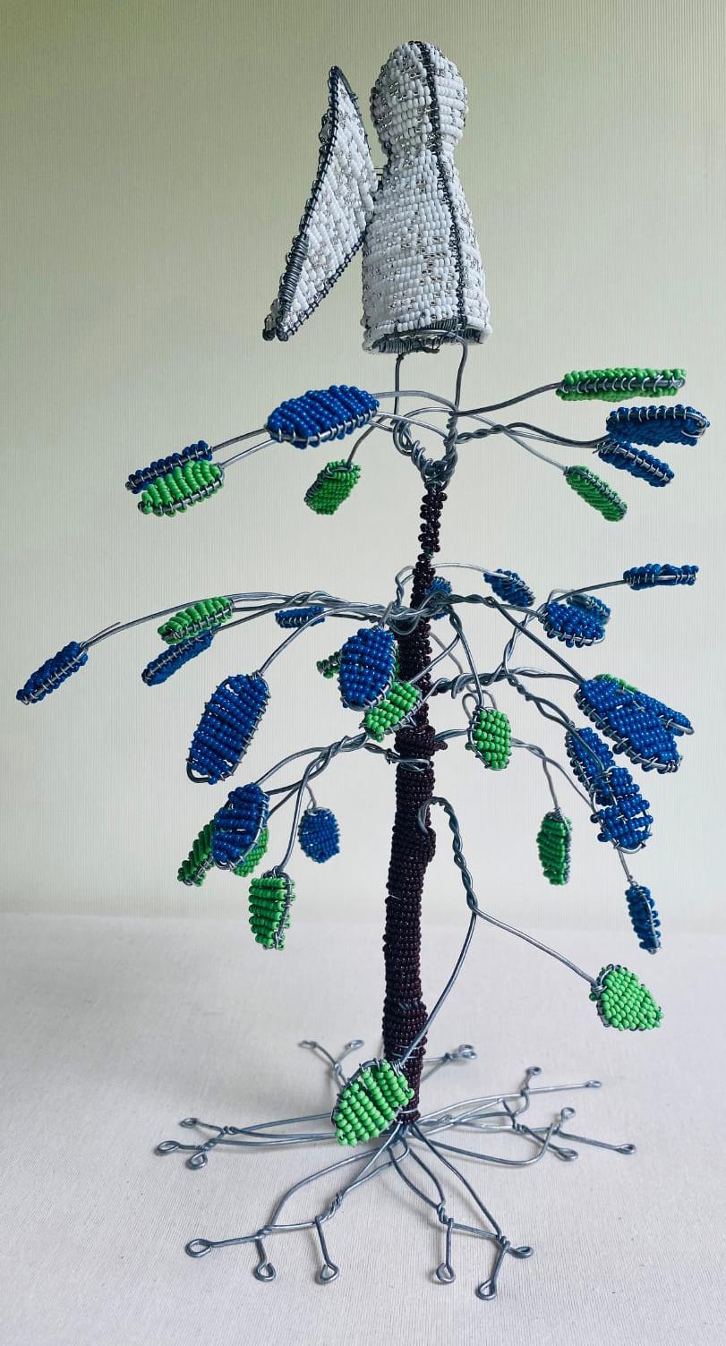A wire sculpture of a tree with blue and green beaded leaves. Inspired by Contra.Joburg, an angelic figure with white beaded wings stands atop, the twisted branches and roots expressing the Weight of Silence through vibrant beadwork.