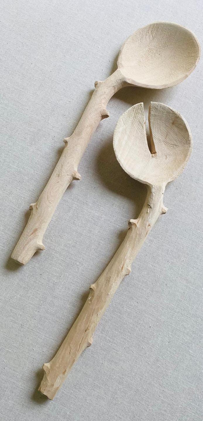 Two wooden salad servers with handles resembling natural, textured branches lay side by side on a light fabric surface—echoing the organic aesthetic found in Contra.Joburg's Weight of Silence collection.