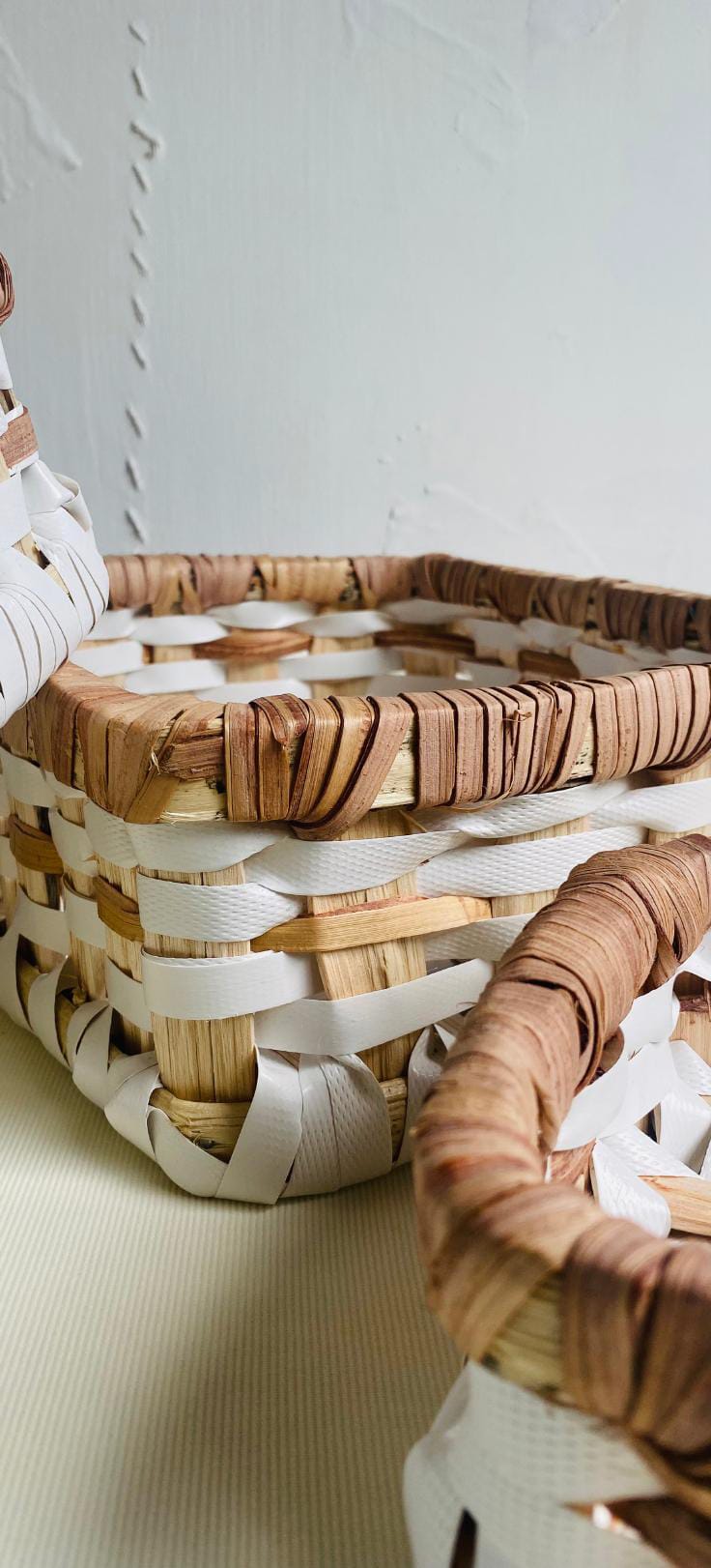 Close-up of two woven baskets with square shapes, made from natural brown and white materials. Featuring tightly wrapped rims and alternating bands, this Contra.Joburg piece highlights intricate craftsmanship against a plain, light background.