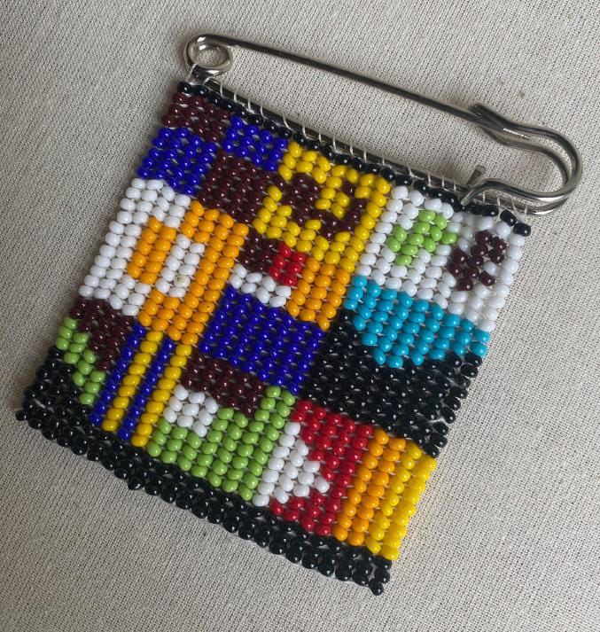 A colourful beaded pin from Contra.Joburg rests on a white surface.