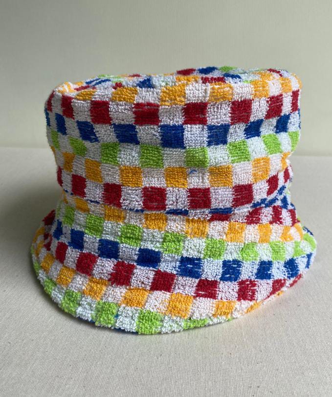 A bucket hat made of textured fabric featuring a colourful chequerboard pattern with alternating squares of red, blue, yellow, and green on a white background—an eye-catching piece inspired by the playful spirit of Contra.Joburg.