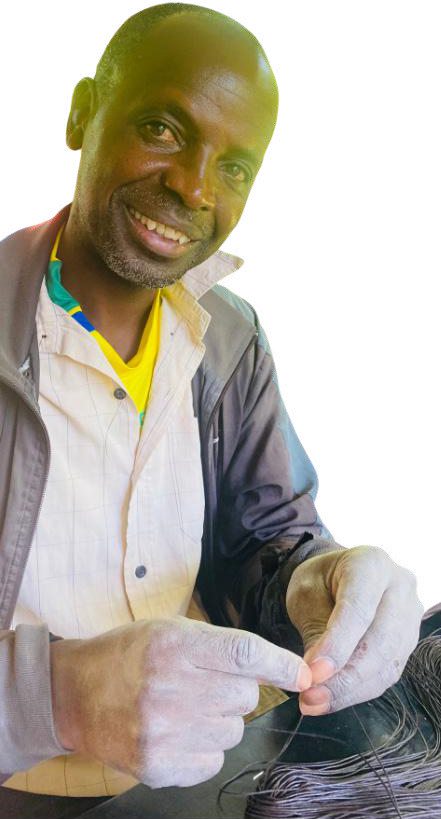 A smiling man in a jacket and yellow shirt sits against a white background, holding thin black wires in his hands. He looks directly at the camera, focused and content—a moment from the Weight of Silence series by Contra.Joburg.