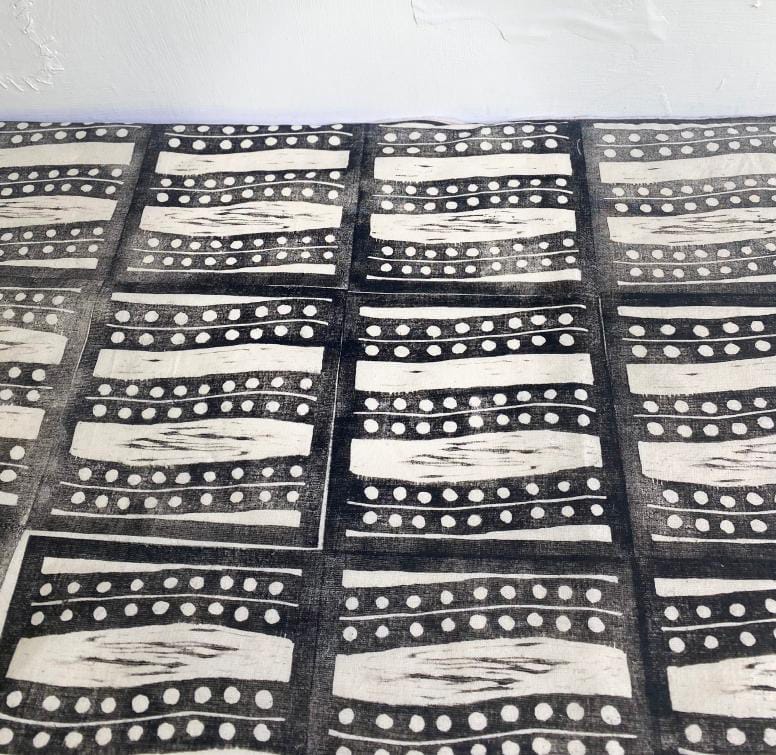 A fabric with a repeating black and white geometric pattern, inspired by Weight of Silence. Each rectangle features wavy lines and dotted rows in a grid across the surface. The white textured background evokes the style of Contra.Joburg.