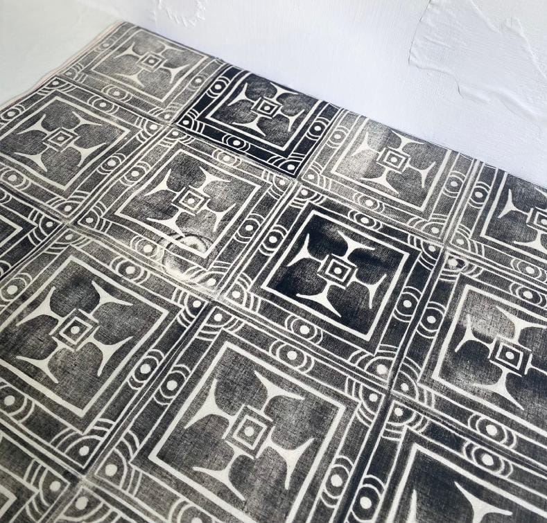 A tabletop from Contra.Joburg featuring black and white geometric tiles with a symmetrical floral and square pattern. The tiles have a slightly distressed, vintage look, and the wall behind them is textured and painted white.