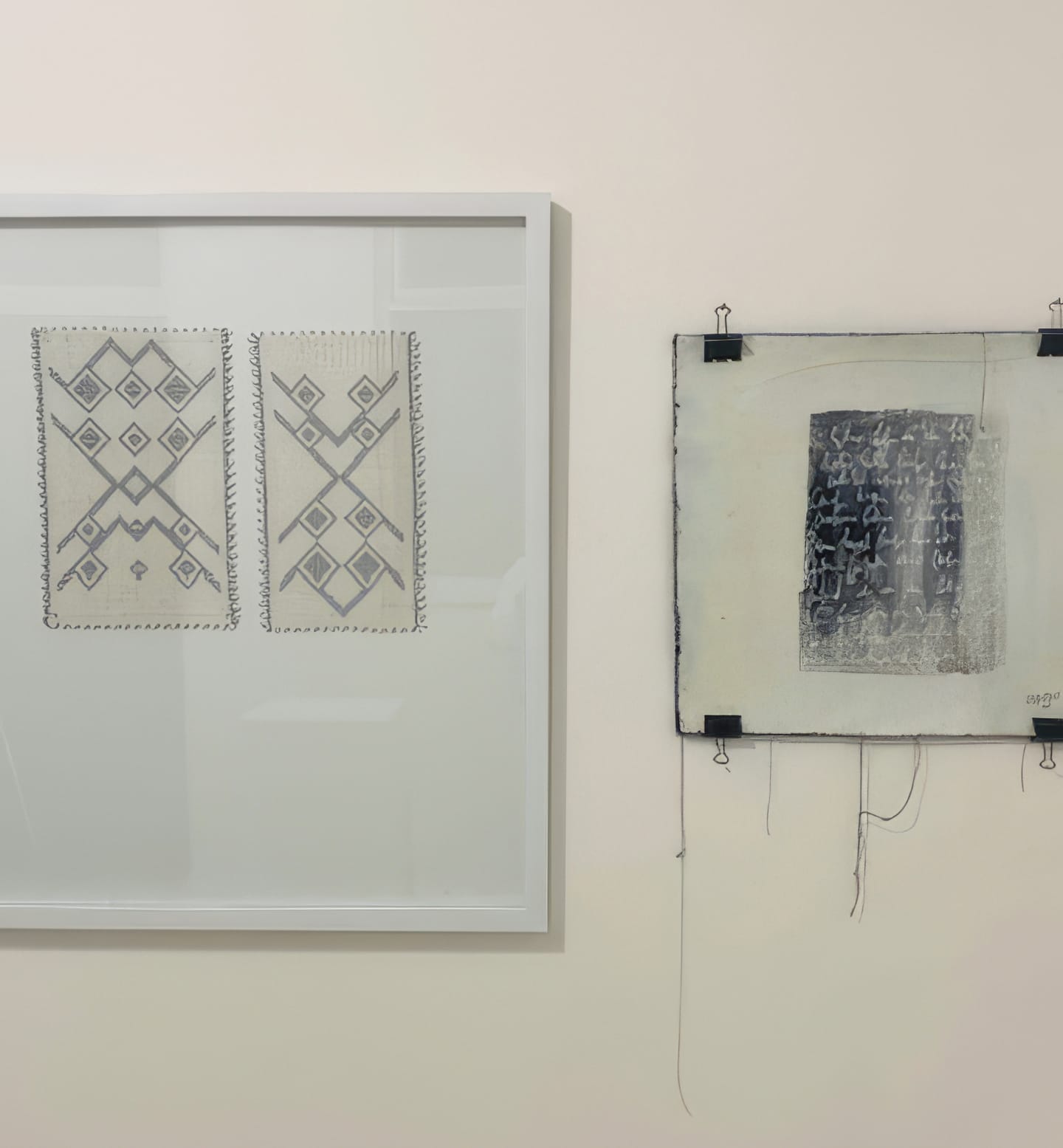 Two framed artworks hang on a white wall at Contra.Joburg. The left piece shows geometric, symmetrical patterns, whilst the right, titled Weight of Silence, features abstract dark markings with loose threads and black clips.