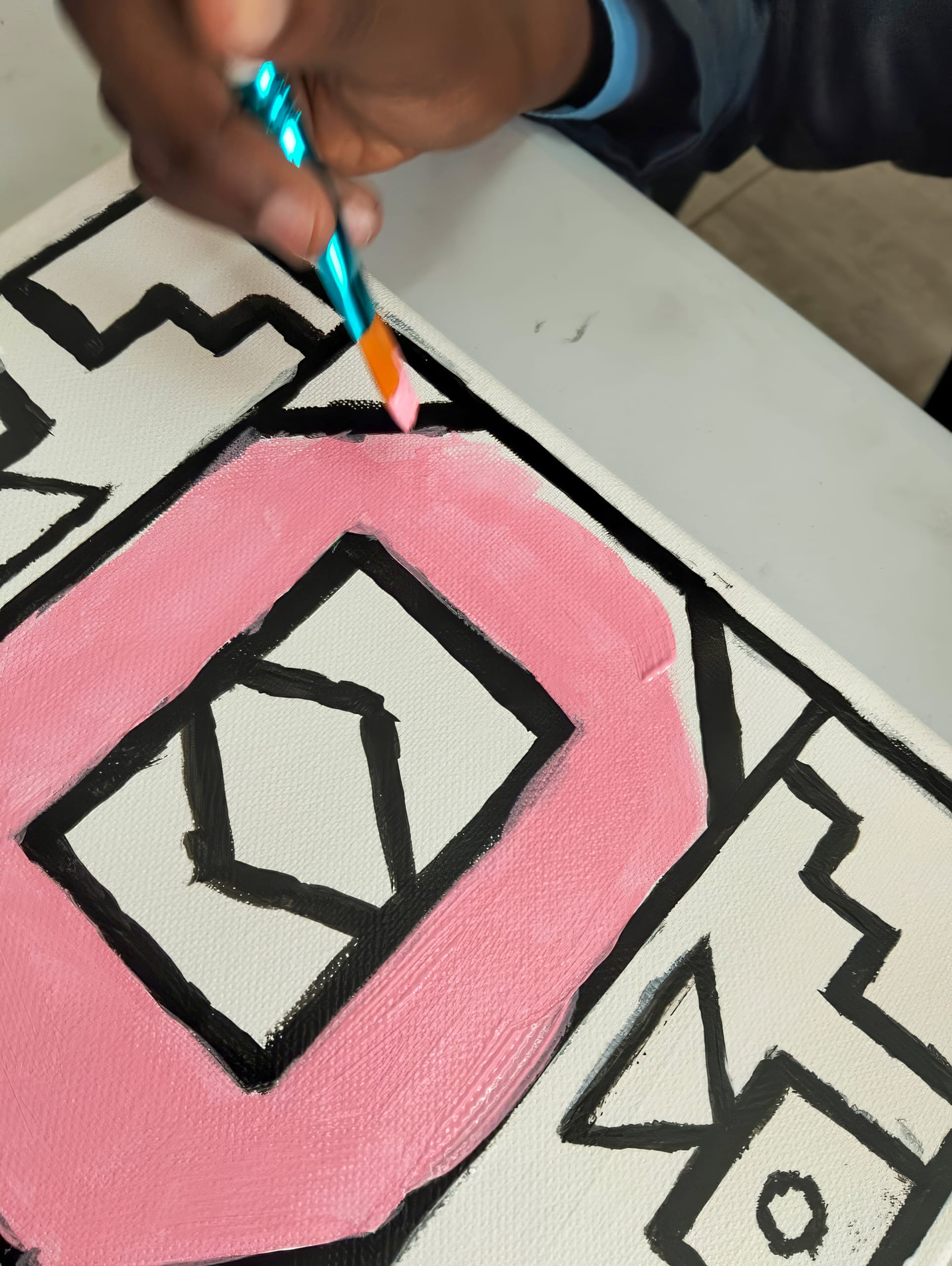 A hand holds a blue paintbrush, painting a large pink letter 