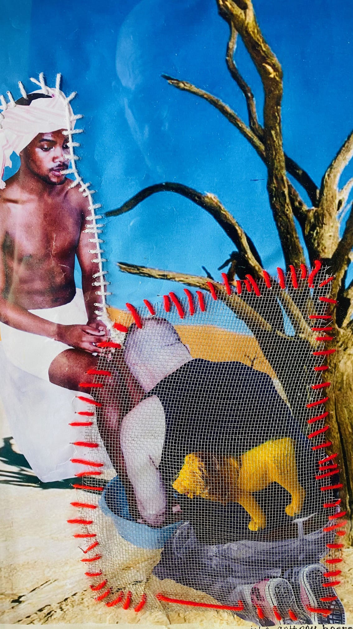 A collage shows a bare-chested man in white cloth sitting on sand near a barren tree, set against a blue sky. In front, an overlay with red stitching depicts a crouched figure with a yellow animal, separated by a mesh screen.